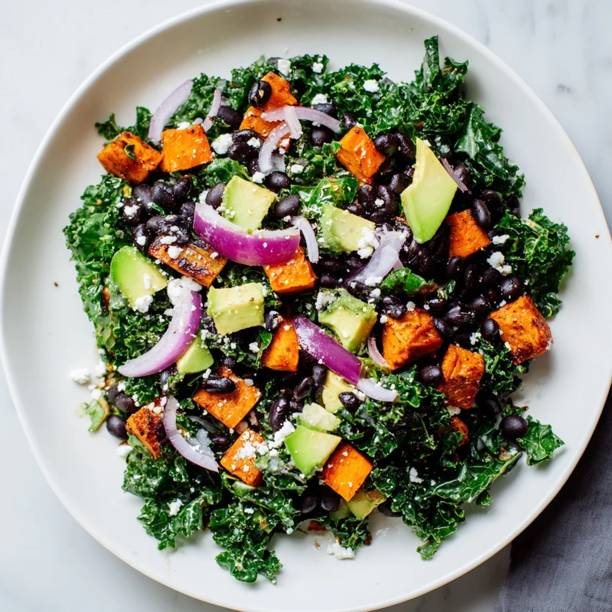 A colorful bowl of fresh Massaged Kale Salad with chunks of sweet potato and creamy avocado.