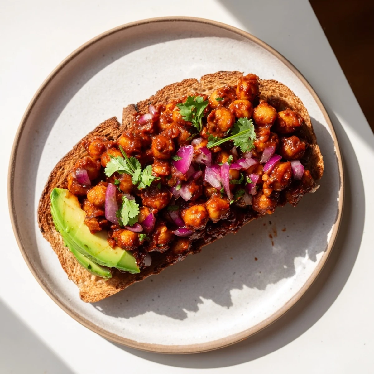 Golden-brown whole grain toast piled high with smoky BBQ chickpeas, garnished fresh cilantro and ready to eat.