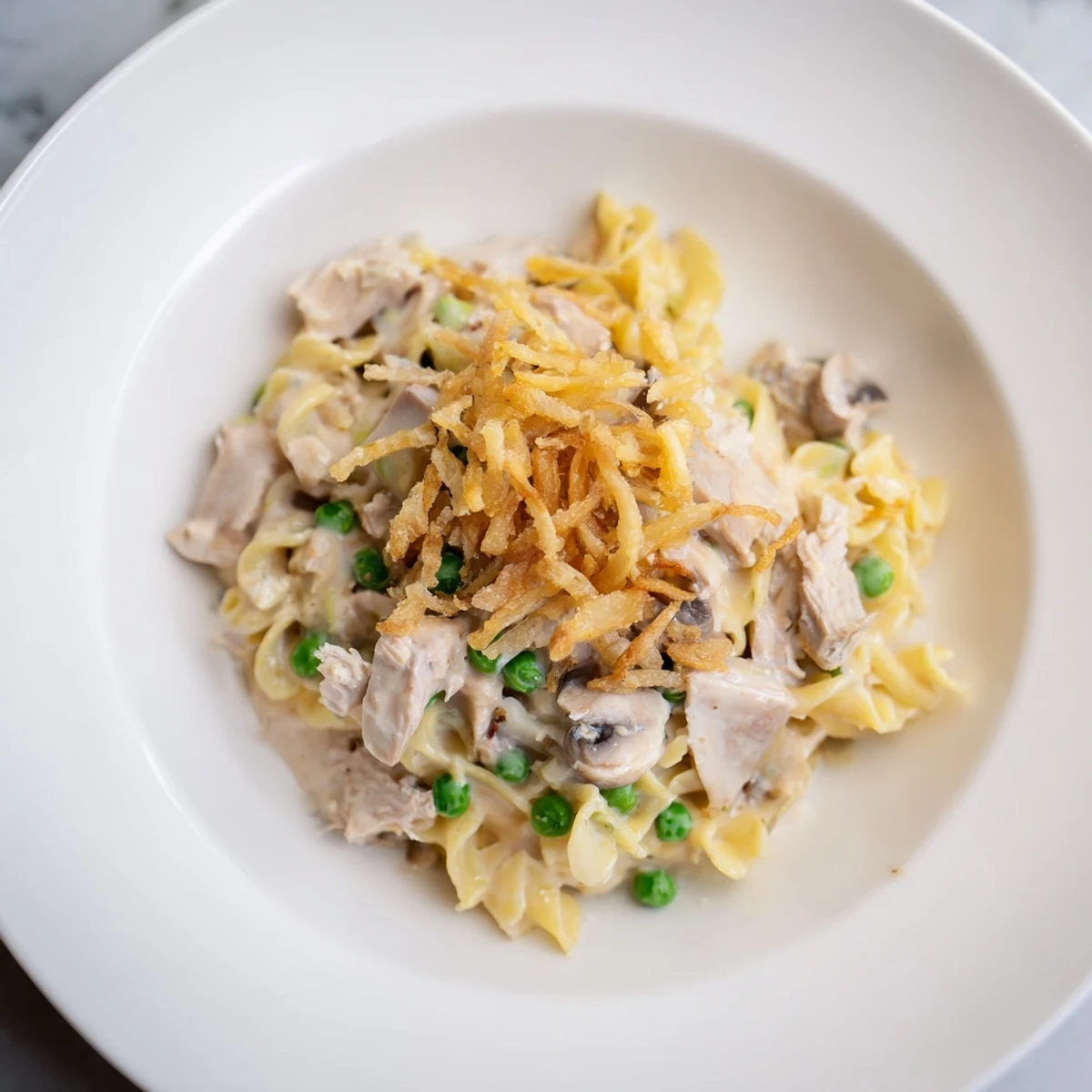 A close-up shot of creamy Homemade Tuna Noodle Casserole, bubbly and inviting with golden-brown fried onions.