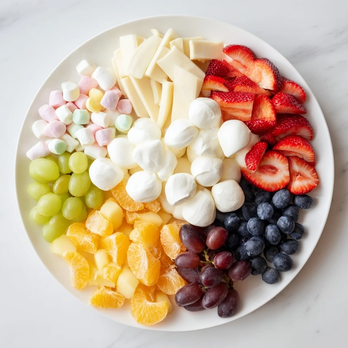 A vibrant Cloud & Rainbow Grazing Board, featuring a rainbow of fresh fruit and creamy cheeses, perfect for parties.