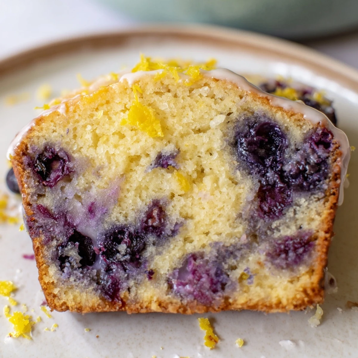A slice of fresh Lemon Blueberry Yogurt Loaf with a drizzle of glaze, perfect for a sunny breakfast.