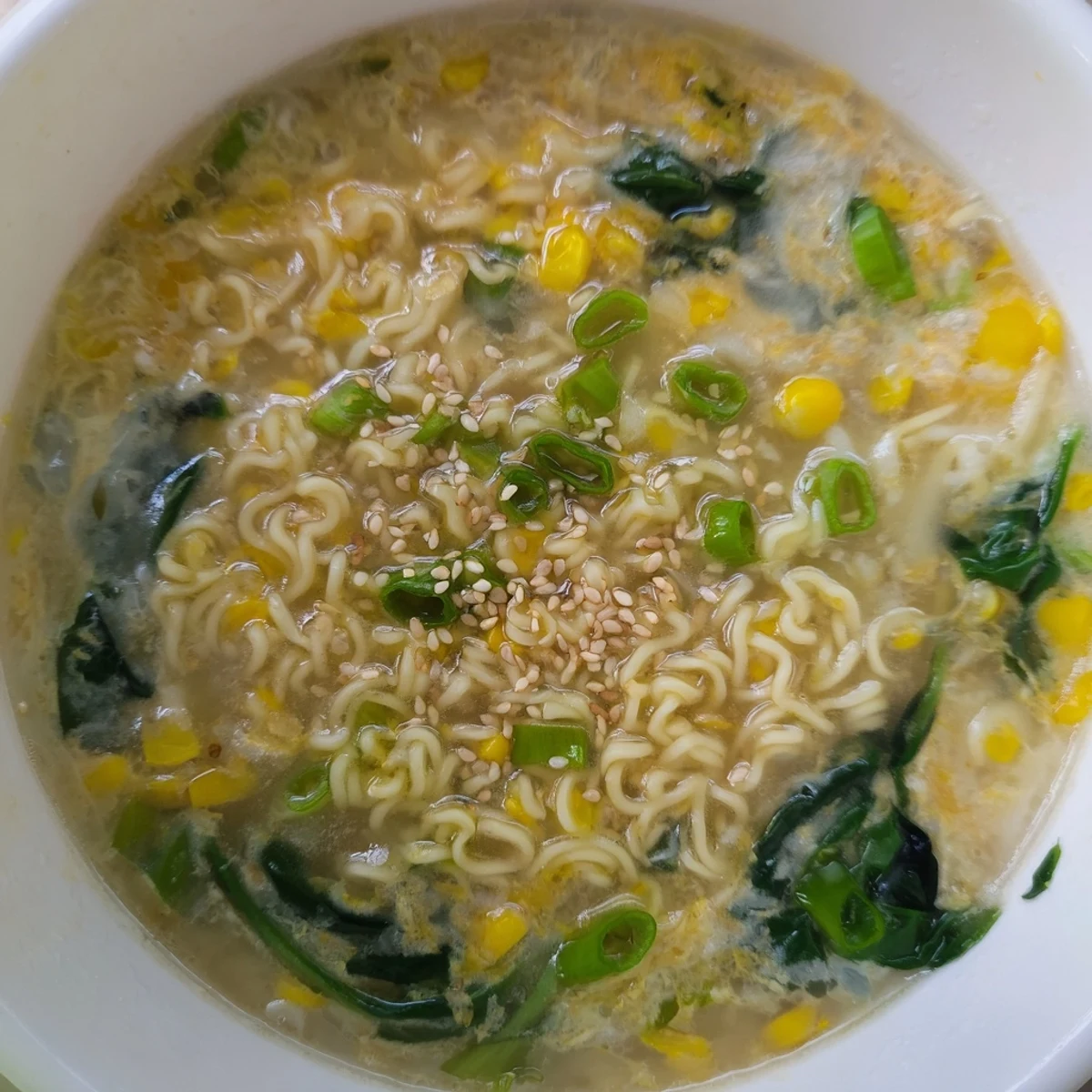 Steaming Elevated Ramen Egg Drop Soup topped with sesame seeds, corn, and wilted spinach, served in a ceramic bowl.