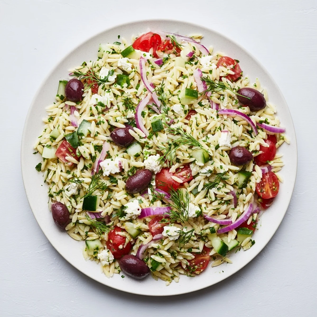 Close-up of Greek Orzo Salad featuring tender orzo pasta, briny Kalamata olives, red onion, fresh parsley, and dill, making a refreshing vegetarian side dish.