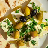 A delicious Turkish olives & cheese board with creamy cheese, green olives, honey, and toasted pita for dipping.