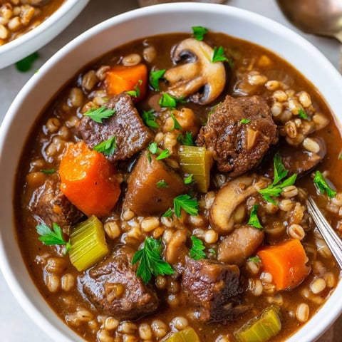 A steaming bowl of hearty beef and barley stew, filled with vibrant vegetables.  