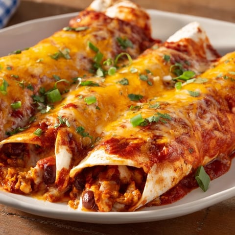 Steaming-hot Cheesy Bean Enchiladas bubbling with melted cheddar cheese and rich red sauce.
