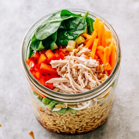 A single-serving Mason Jar Noodle Meal Prep showcases layered ramen, colorful peppers, and fresh spinach in a clear jar.  
