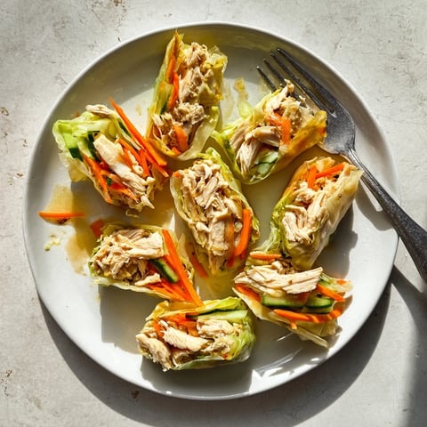 Golden-brown garlicky pulled chicken wraps resting on a rustic wooden board, revealing tender shredded chicken inside the crisp rice paper.