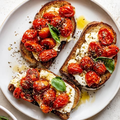 Golden, baked feta toast with roasted cherry tomatoes on crispy sourdough, topped with fresh basil for a Mediterranean snack.