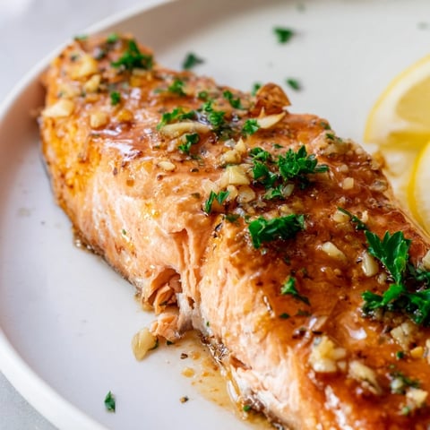 Roasted honey garlic glazed salmon fillets glistening with a golden, sticky glaze on a rustic serving platter with lemon wedges.