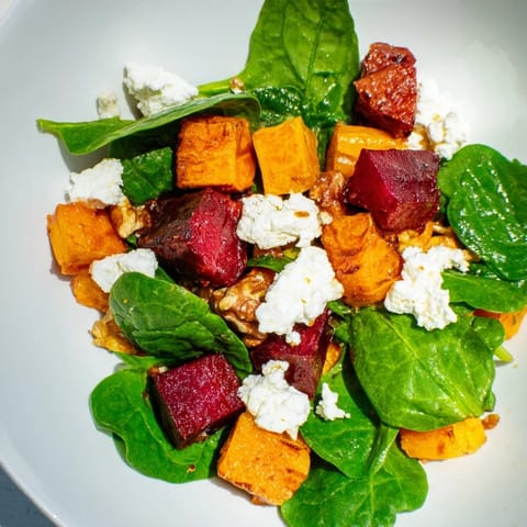 A beautiful bowl of the roasted beet & butternut squash salad with vibrant leaves and goat cheese.