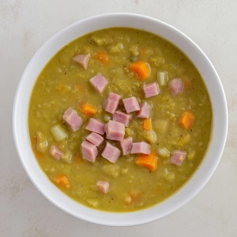 A close-up shot of rich Hearty Split Pea and Ham Soup with visible ham and vegetables simmering.
