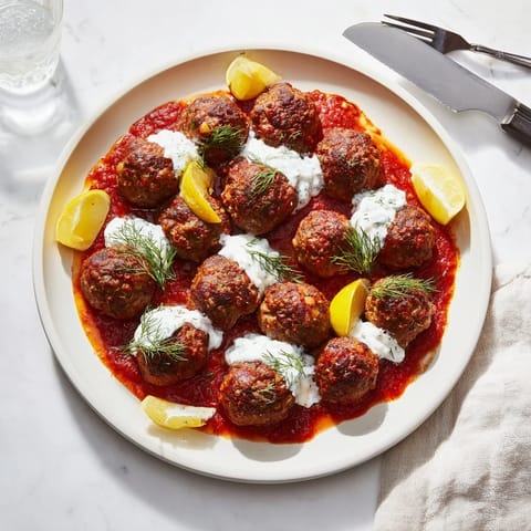Close-up of tender Instant Pot Greek-Style Meatballs, smothered in creamy feta-lemon sauce and fresh herbs.