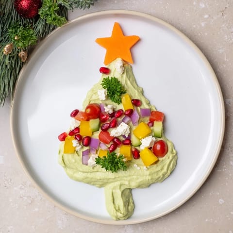 Vivid green whipped avocado shaped as a Christmas tree, decorated for a delicious holiday appetizer.