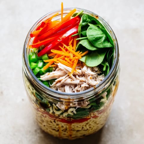 Bright, appetizing close-up of a Mason Jar Noodle Meal Prep with tofu, bean sprouts, and chopped peanuts on top.  