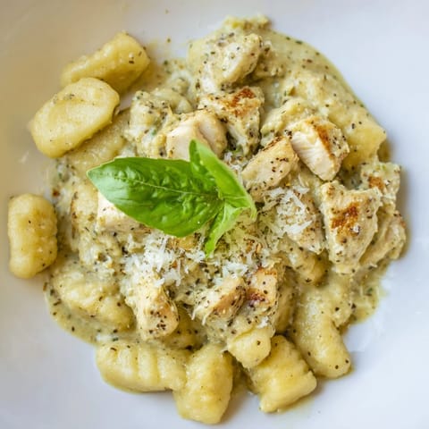 Savory Creamy Pesto Gnocchi with Chicken steaming in a skillet, garnished with fresh basil and grated Parmesan cheese.