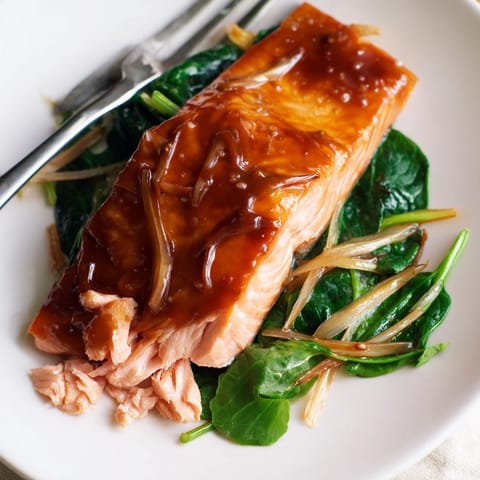 A close-up of miso salmon atop sautéed spinach, highlighting the caramelized glaze and tender green leaves.  
