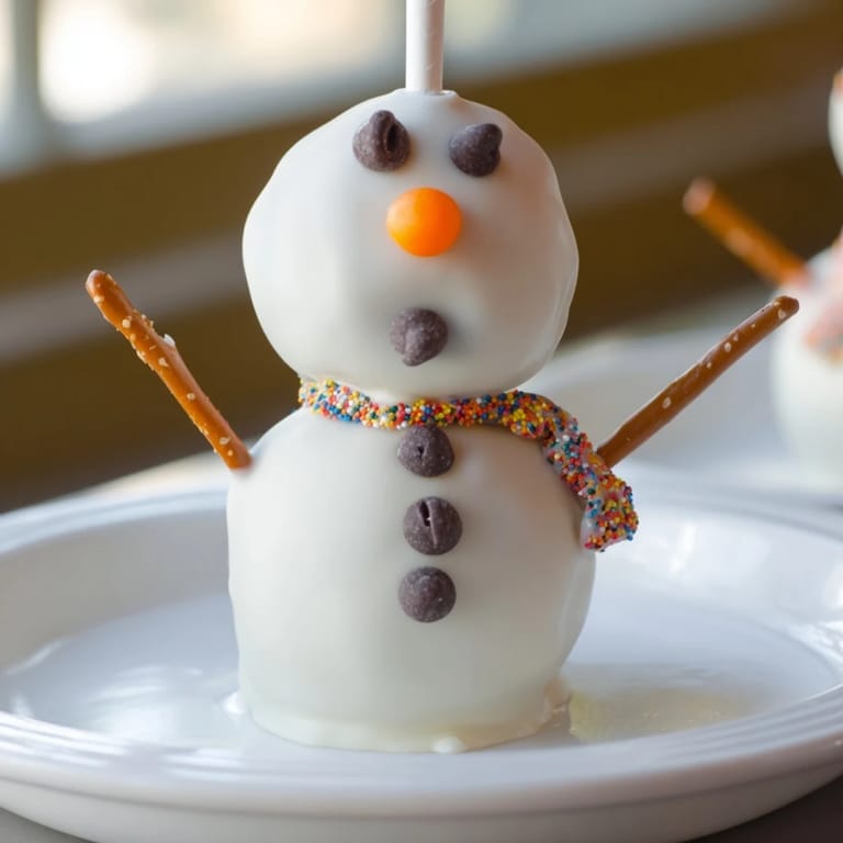 Festive Oreo Snowman Cake Pops, decorated with chocolate chips and pretzel arms, perfect for a party.