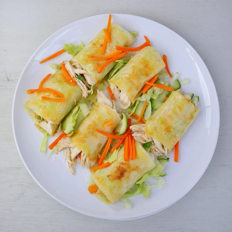 Freshly cooked garlicky pulled chicken wraps arranged on a white ceramic platter with lemon wedges and a side of dipping sauce.