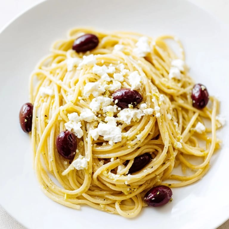 Tossed Greek Chicken Spaghetti with sautéed garlic, red onion, and tangy dressing, served with a glass of crisp white wine.