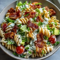 A colorful BLT pasta salad with bacon, avocado, and cherry tomatoes tossed in a creamy dressing, perfect for summer picnics.